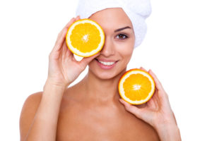 A young girl takes spa treatments with oranges in hand. White background.